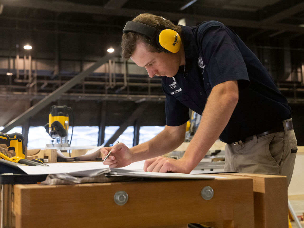 An Australian competitor in WorldSkills Competition 2022 Special Edition leans over a bench to look at plans at Holz, Switzerland’s woodworking sector trade fair, at Messe Basel, Switzerland from 11 to 14 October.
